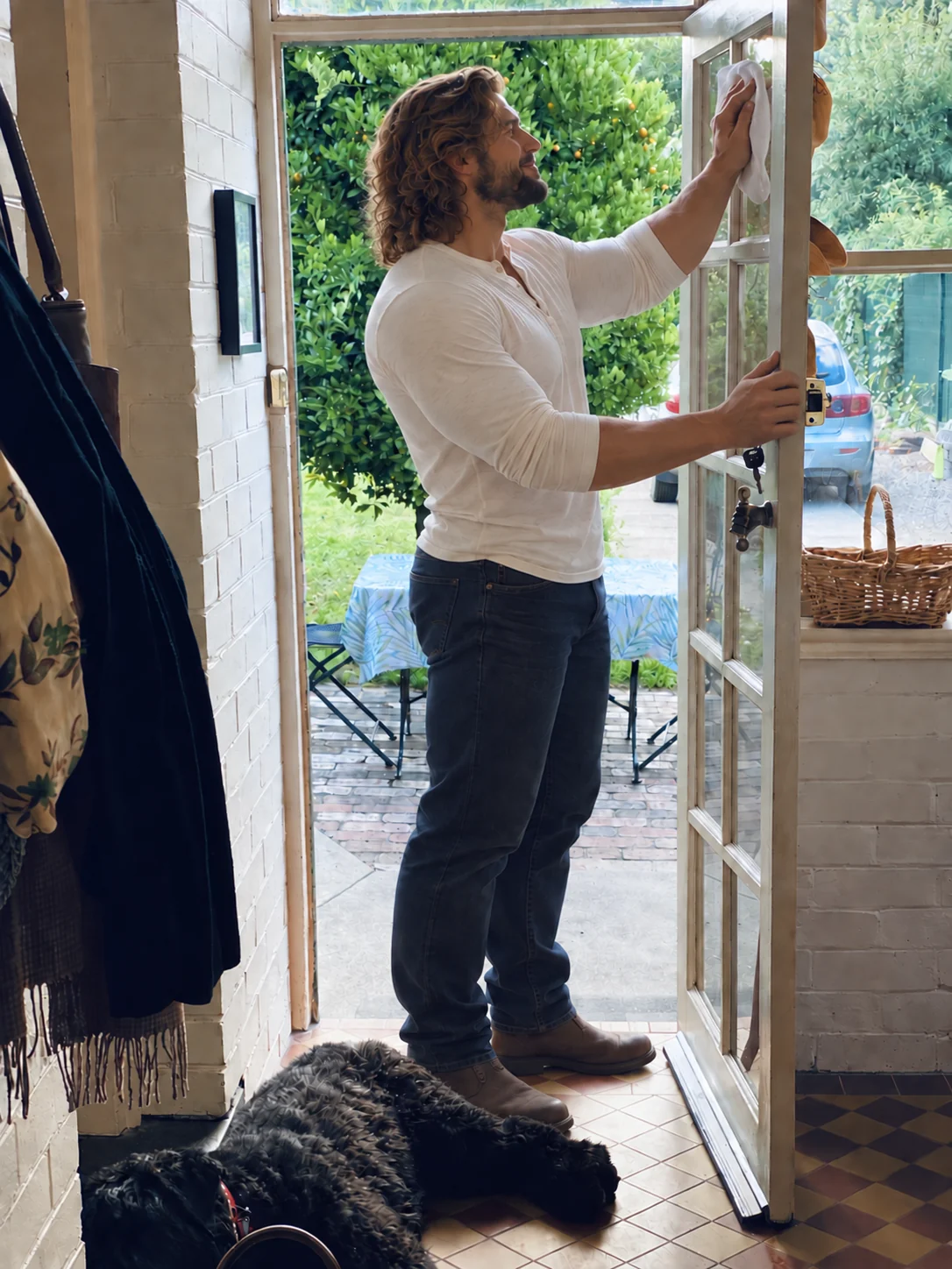 Husband cleaning the glass of a doorway, with a table waiting outside